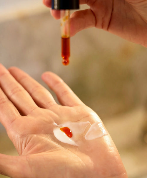 drop of orange liquid astaxanthin booster, from VRESERVE dropping into a palm of someone with cream in it.