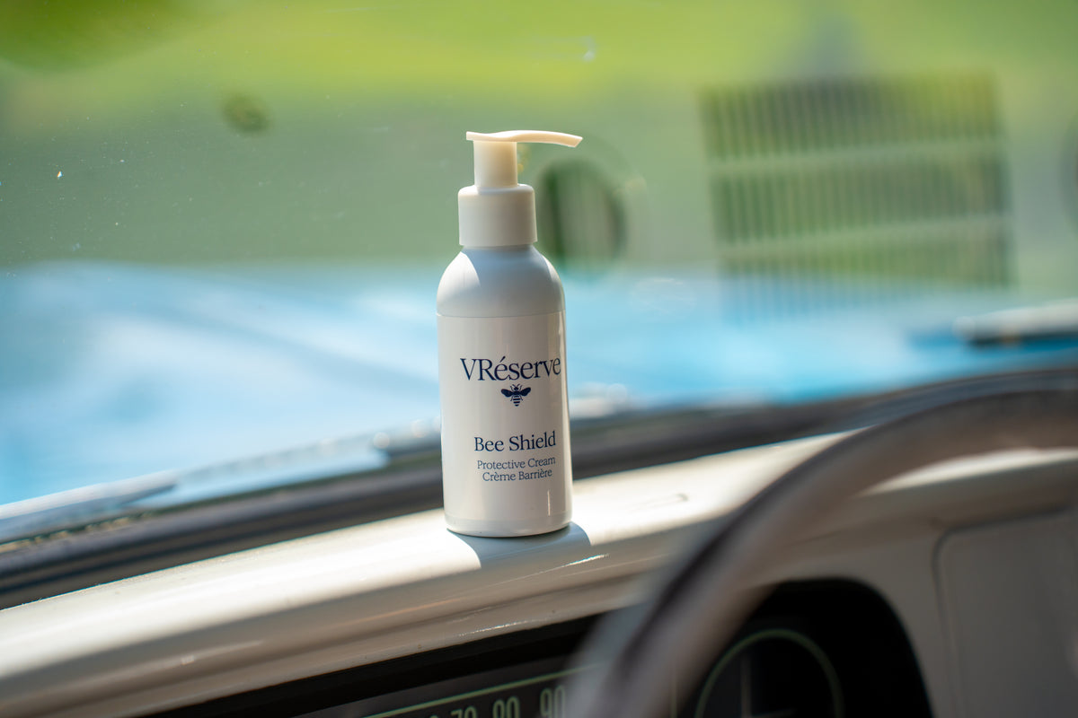A white pump bottle of VReserve Bee Shield lotion resting on the dashboard of a car, with the windshield and blurred outdoor scenery in the background.