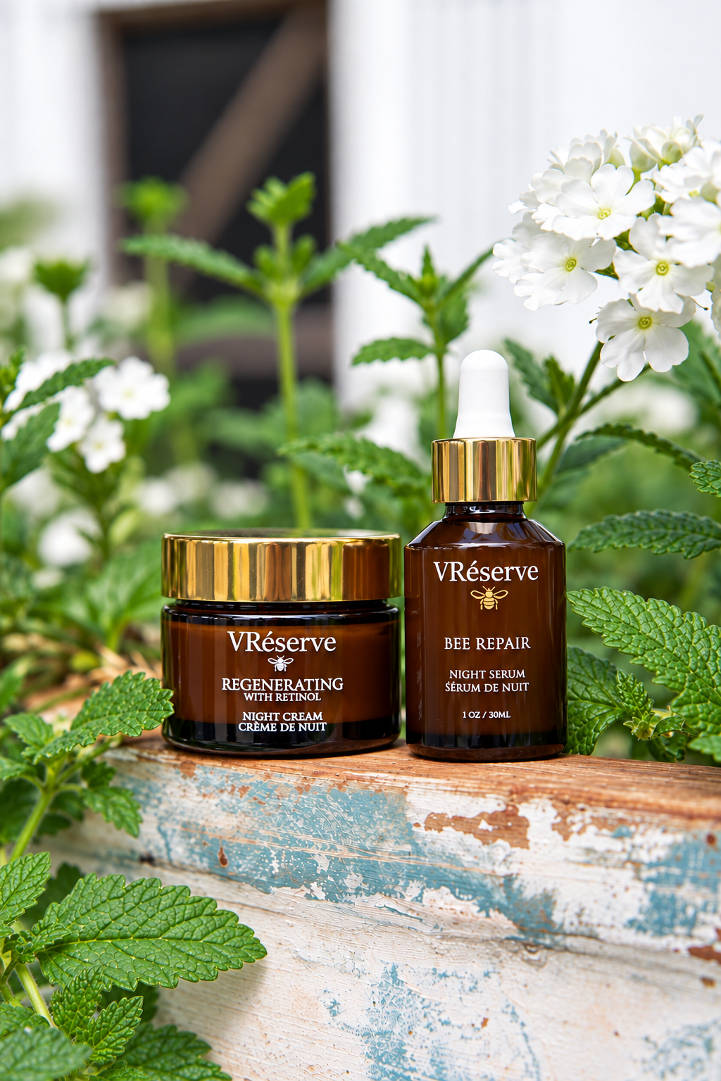 Two VRéserve skincare products, a brown jar of Regenerating Night Cream and a brown dropper bottle of Bee Repair Night Serum, displayed on a weathered blue wooden ledge surrounded by green leaves and white flowers.