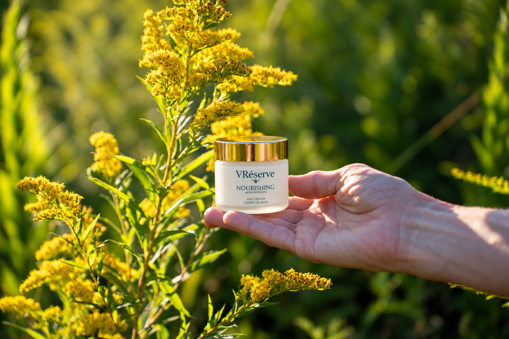 A hand holds a small white cosmetic jar labeled VRéserve Nourishing Moisturizer against a natural outdoor background of green foliage and yellow flowers.