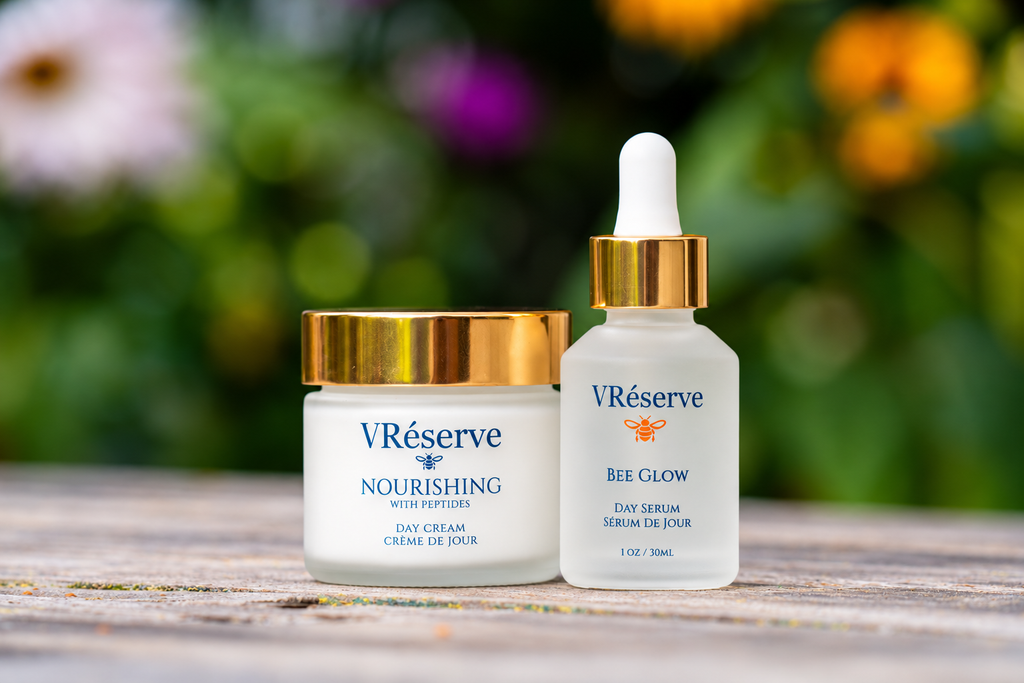 Two VRéserve skincare products, 'Nourishing' Day Cream and 'Bee Glow' Day Serum, displayed side-by-side on a rustic wooden surface with a blurred garden background.