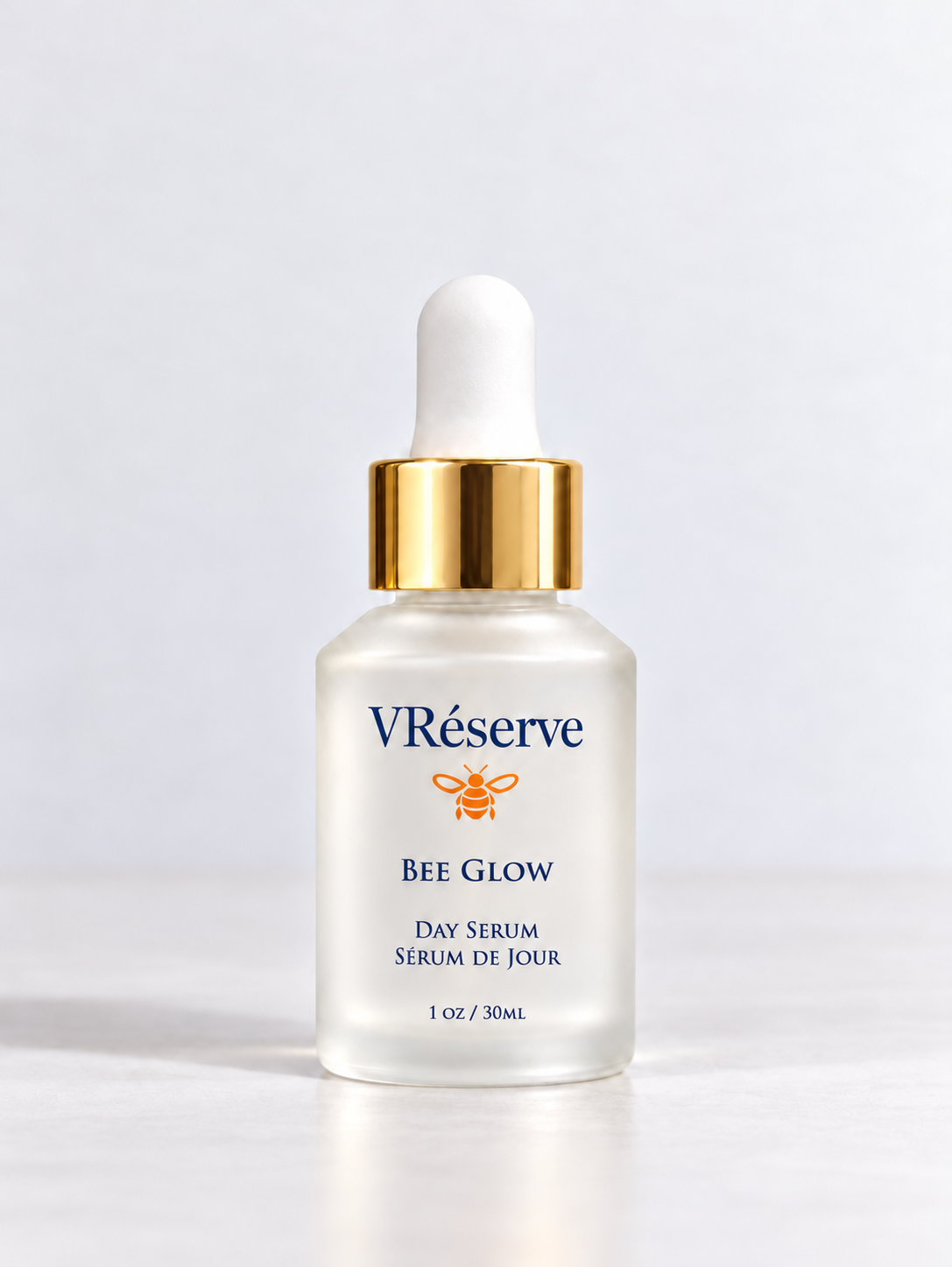 A bottle of VRéserve Bee Glow Day Serum with a white dropper cap, gold collar, and frosted glass bottle on a light gray background.