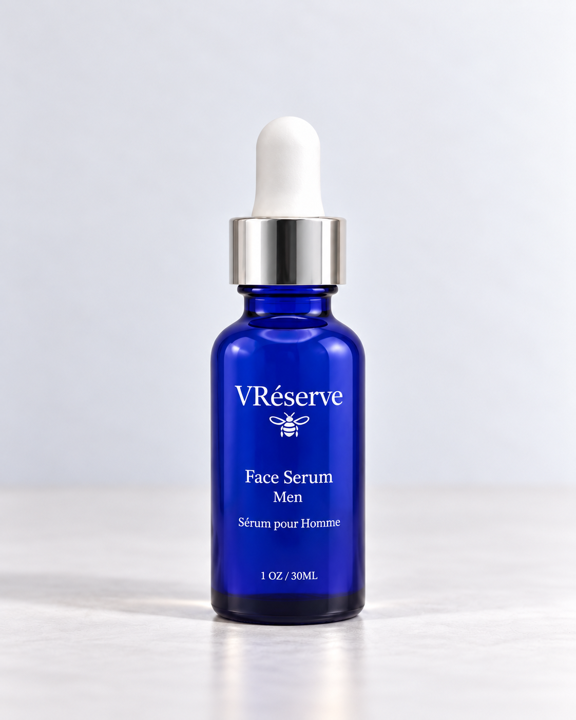 A cobalt blue glass dropper bottle of VRéserve Face Serum Men with a white rubber bulb and a shiny silver collar, set against a clean light gray background.